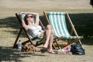 Soaking up the sun: One woman makes the most of the warm weather as she reclines on a deck chair in Hyde Park, London today